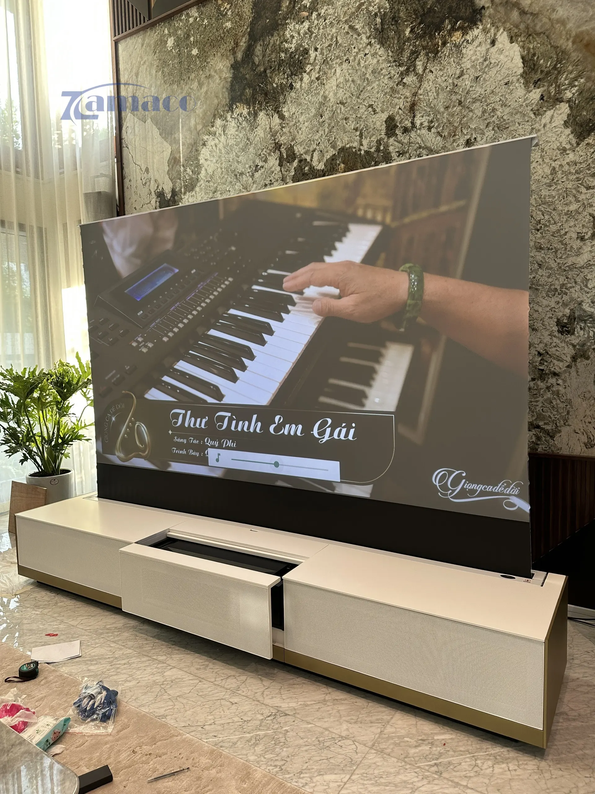 Hệ thống máy chiếu siêu gần Epson EH-LS800B được lắp đặt trong tủ TV Laser New York, trình chiếu hình ảnh 120 inch trên màn chiếu quang học Vividstorm để sàn trong không gian phòng khách hiện đại.